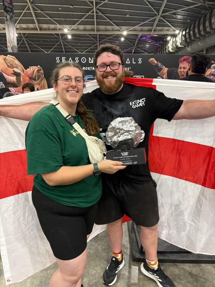 Two people stand next to each other one of which holds a trophy and the other holds an England flag behind them Two people stand next to each other one of which holds a trophy and the other holds an England flag behind them