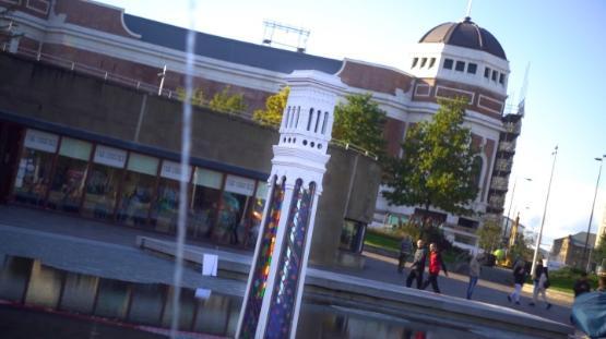 An large art installation is in a small water pool in a city centre with large buildings behind it An large art installation is in a small water pool in a city centre with large buildings behind it