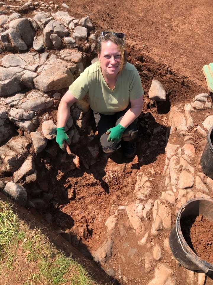 A person on an archaeological dig wearing gloves looks upwards A person on an archaeological dig wearing gloves looks upwards