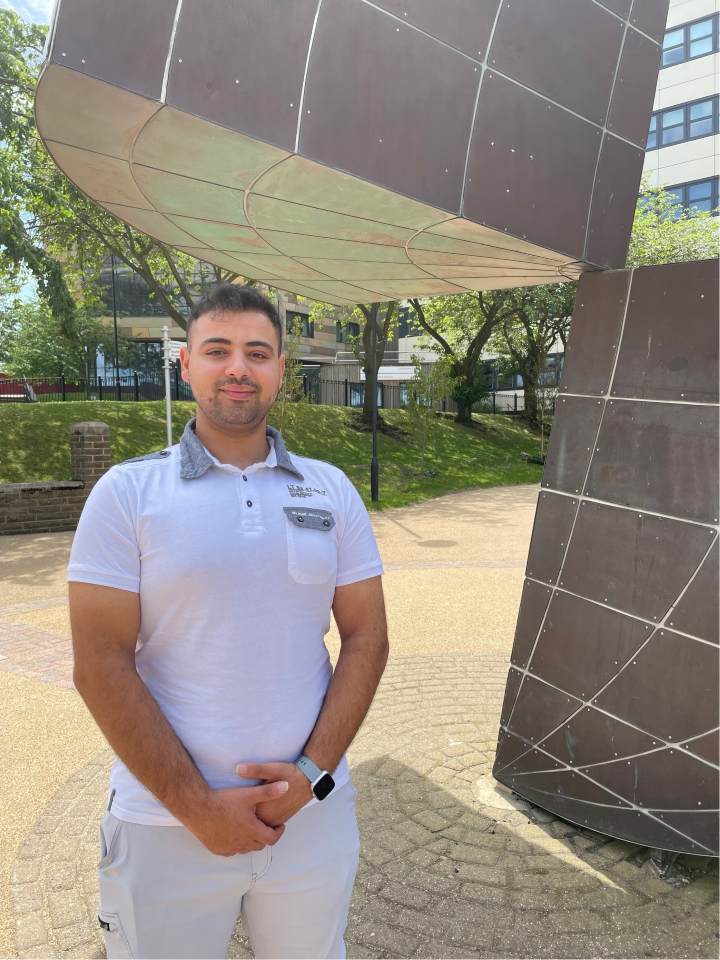 a student in a T-shirt stands next to a sculpture on campus a student in a T-shirt stands next to a sculpture on campus