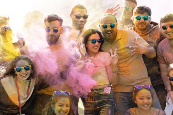 A group of students smiling and covered in pink and orange dusty paint at a party A group of students smiling and covered in pink and orange dusty paint at a party
