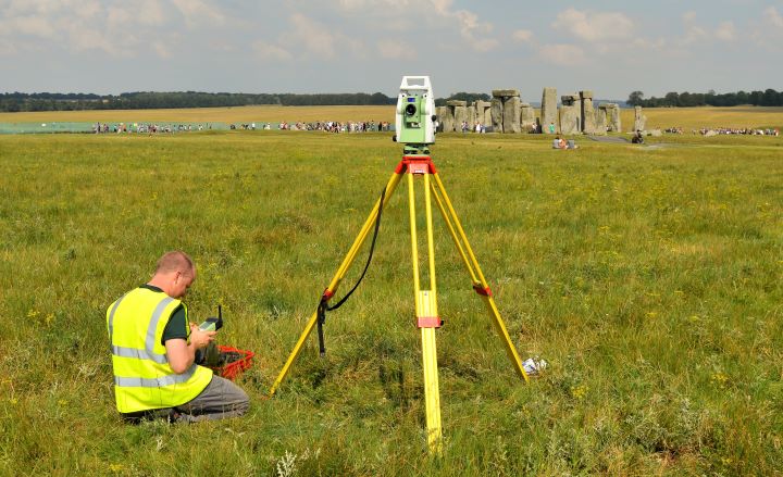 a person sits in a field next to a tripod with a stone monument in the background a person sits in a field next to a tripod with a stone monument in the background