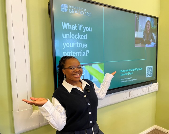 A person smiles with their arms held out to their side in front of video screen A person smiles with their arms held out to their side in front of video screen