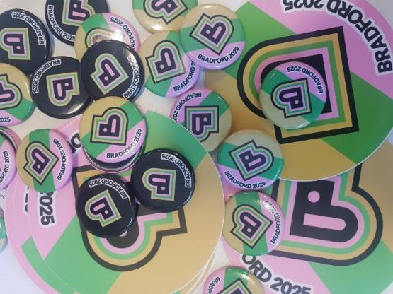 A selection of small Bradford 2025 badges which are coloured pink, green, yellow and black A selection of small Bradford 2025 badges which are coloured pink, green, yellow and black