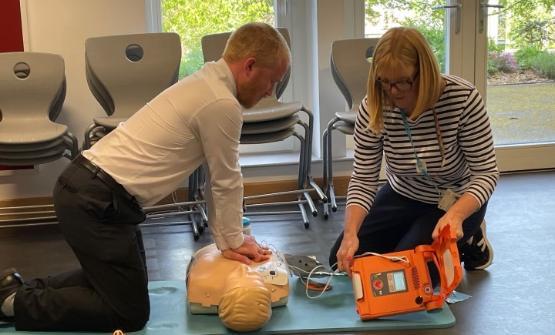 One person using CPR techniques on a dummy as a person next to them holds a defibrillator One person using CPR techniques on a dummy as a person next to them holds a defibrillator