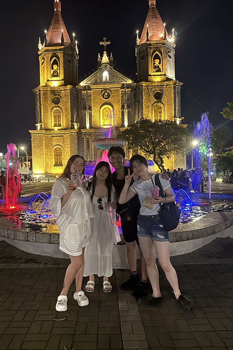 Courtney standing with her friends in front of a lit up building. Courtney standing with her friends in front of a lit up building.