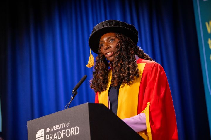 person in graduation gown speaks at a lecturn person in graduation gown speaks at a lecturn