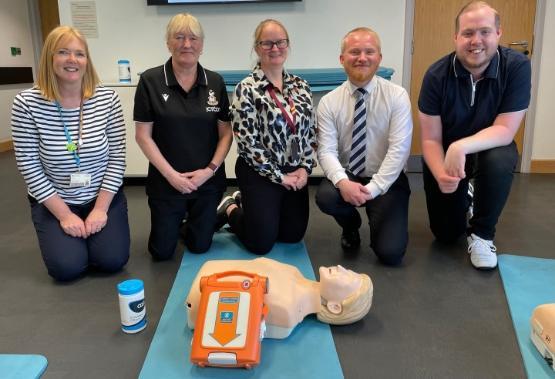 Five people crouched down on their knees behind a CPR dummy Five people crouched down on their knees behind a CPR dummy