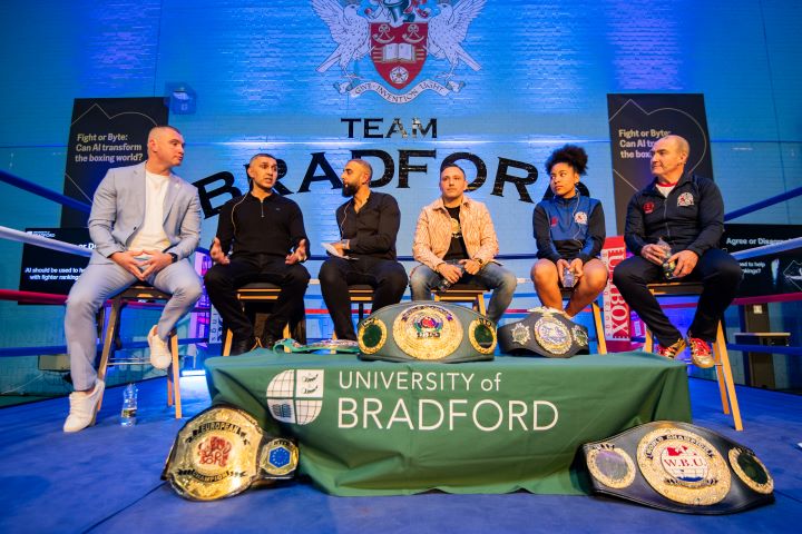 A group of people sat down with a table of boxing belts in front of them A group of people sat down with a table of boxing belts in front of them
