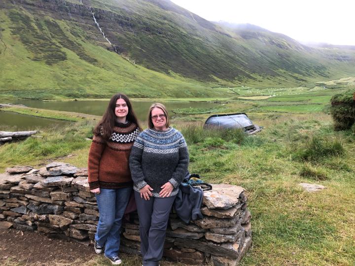 A mother and daughter in jumpers sit on a wall with a mountain backdrop A mother and daughter in jumpers sit on a wall with a mountain backdrop