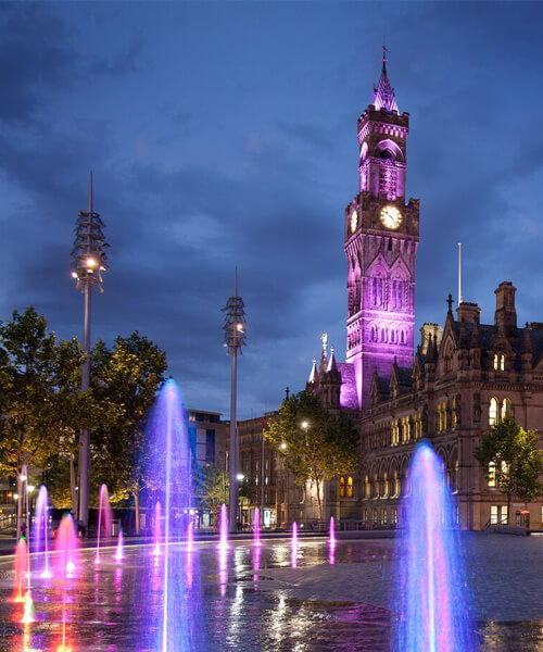Centenary Square, Bradford, at night, the water fountain and clocktower are lit up shades of pink and purple