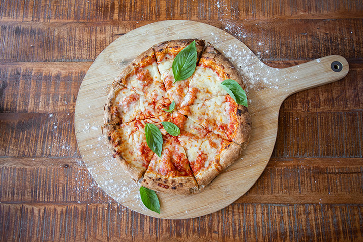 Pizza on a wooden board with basil and flour sprinkled on top