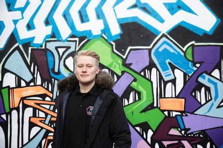 A Bradford student stood smiling in front of a graffiti covered wall