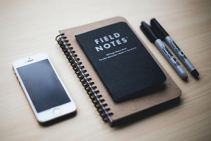 A phone next to a notepad and pens.