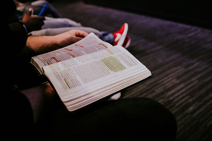 A person reading a highlighted bible on their lap.