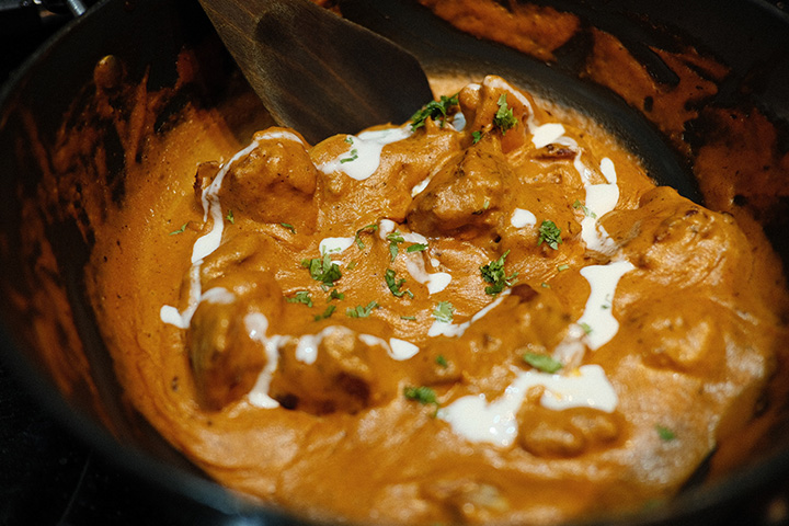 Butter chicken curry in a black pot with a spoon