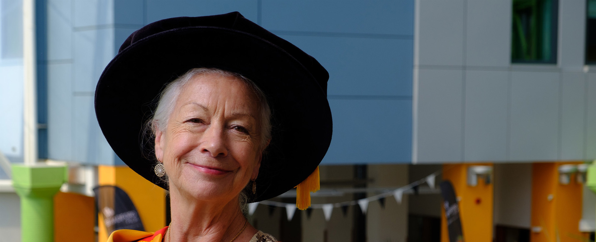 Dr Scillia Elworthy wearing her honorary graduate gown and hat while posing in the atrium of the Richmond Building.