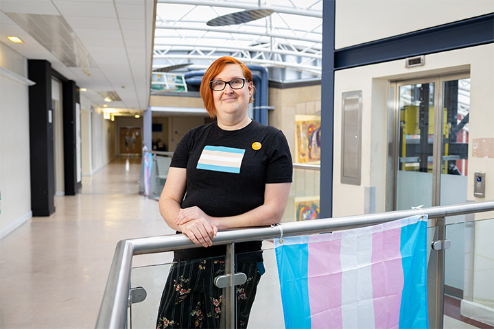 A student holding a trans rights flag in support of the movement smiles at the camera