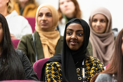 Female students smiling while in attendance at a lecture.