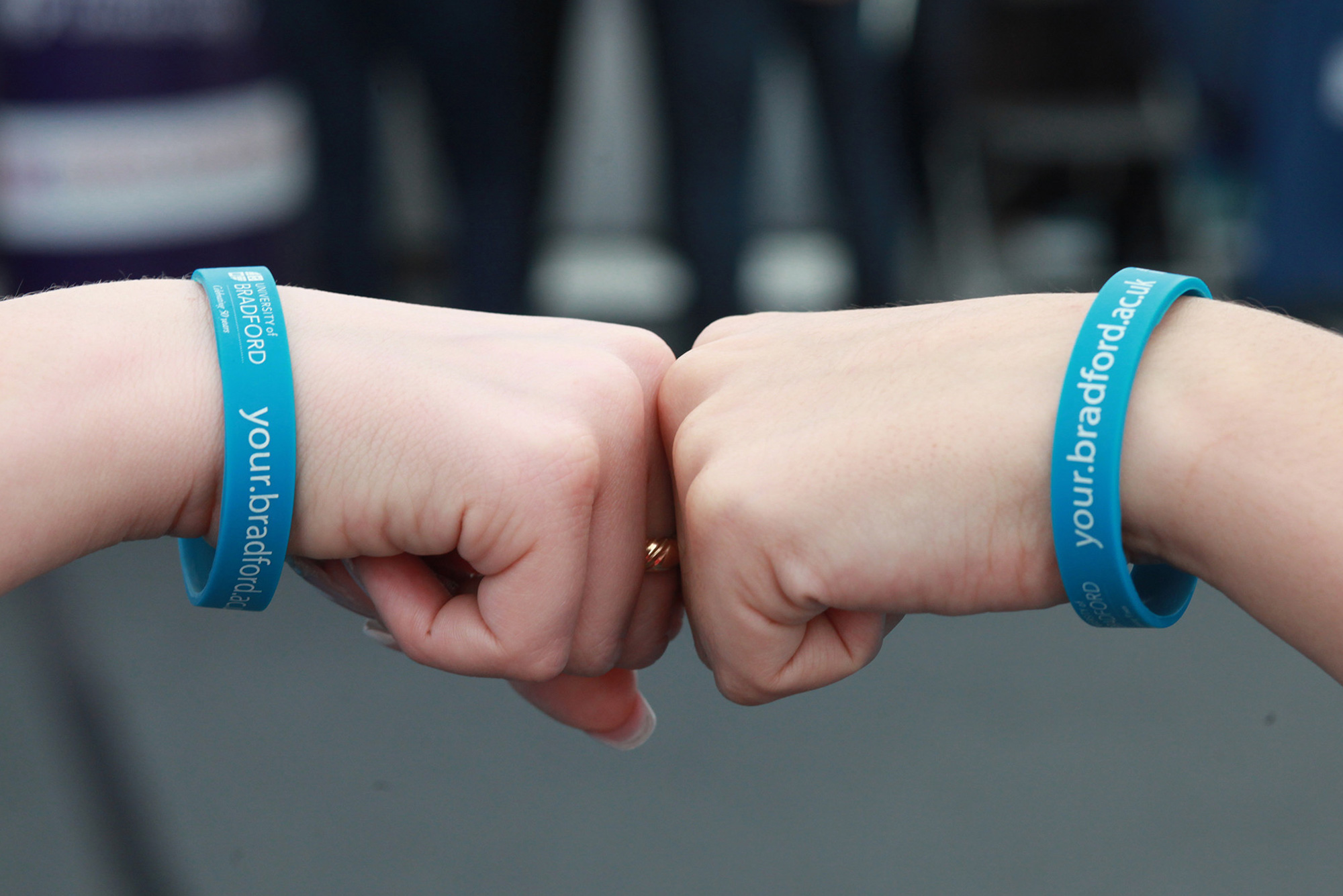 Two people touching fists wearing University of Bradford wristbands