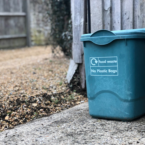 Green food waste bin with a sign on that says No plastic bags.