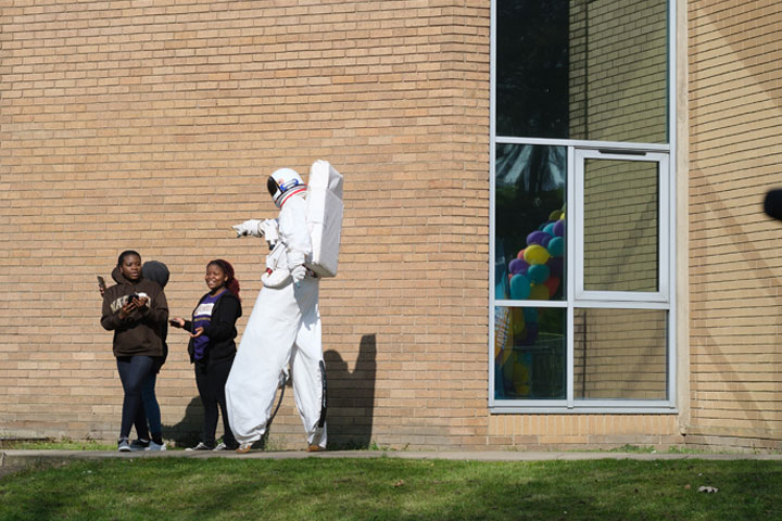 A man on stilts wearing an astronaut costume walking with two ladies