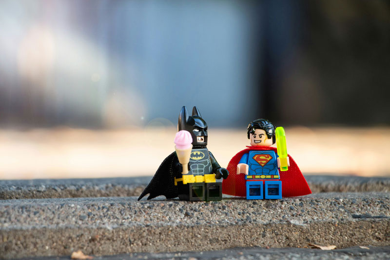 A Lego batman holding a Lego ice-cream and a Lego superman holding Lego lolly