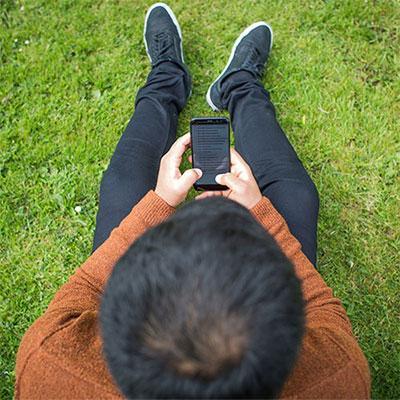 Student sat on grass, looking at their phone.