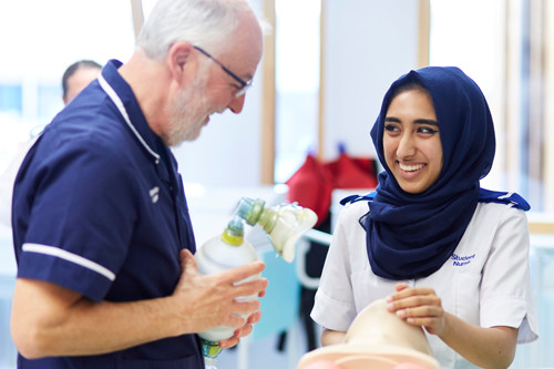 A member of teaching staff and nursing student smiling. The member of staff is holding a CPR resuscitation bag.