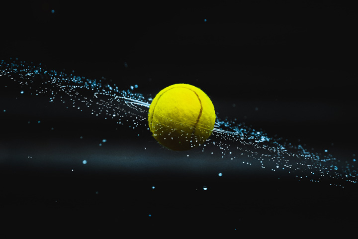 Wet spinning tennis ball with flecks of water coming off it.