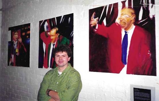 An image of Dr Rob Wilmot aged 26 standing in front of paintings on a wall