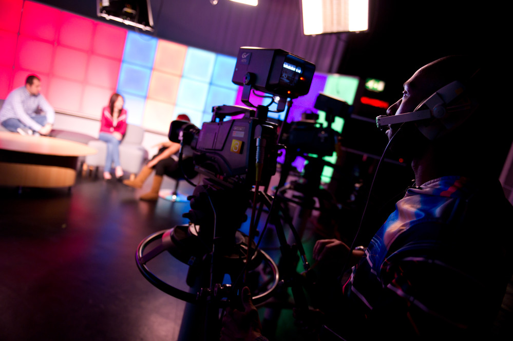 A student filming three students in the University TV studio.