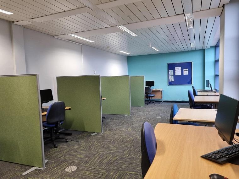 study room containing tables, computers and privacy screens dividing study areas