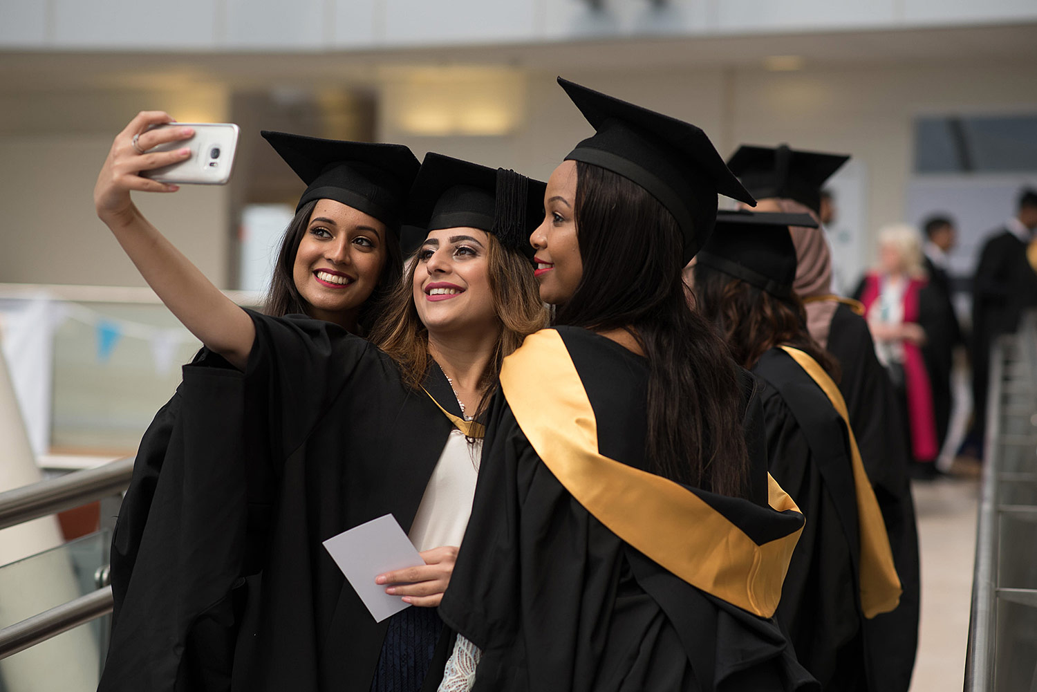 Three students at graduation posing together to take a selfie-photograph.