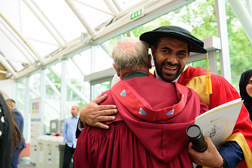 Two people in graduation robes hugging.