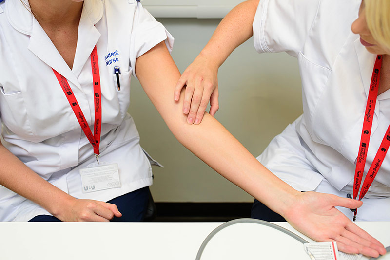 Student nurse examining the arm of another student nurse.