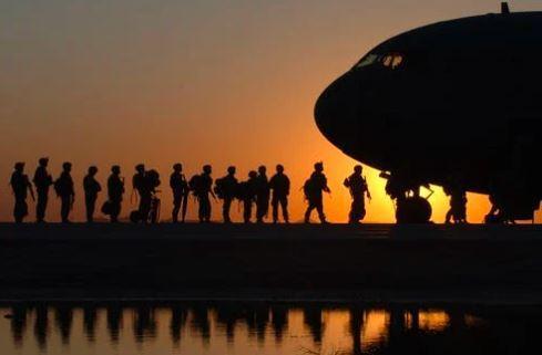 Soldiers boarding a plane, in silhouette against orange sunset