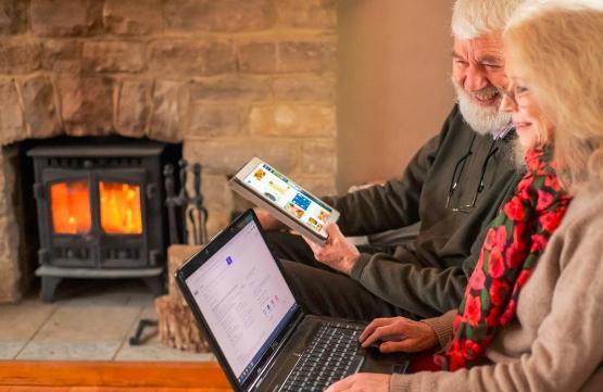 Two older people sat in front of a log burner looking at an ipad