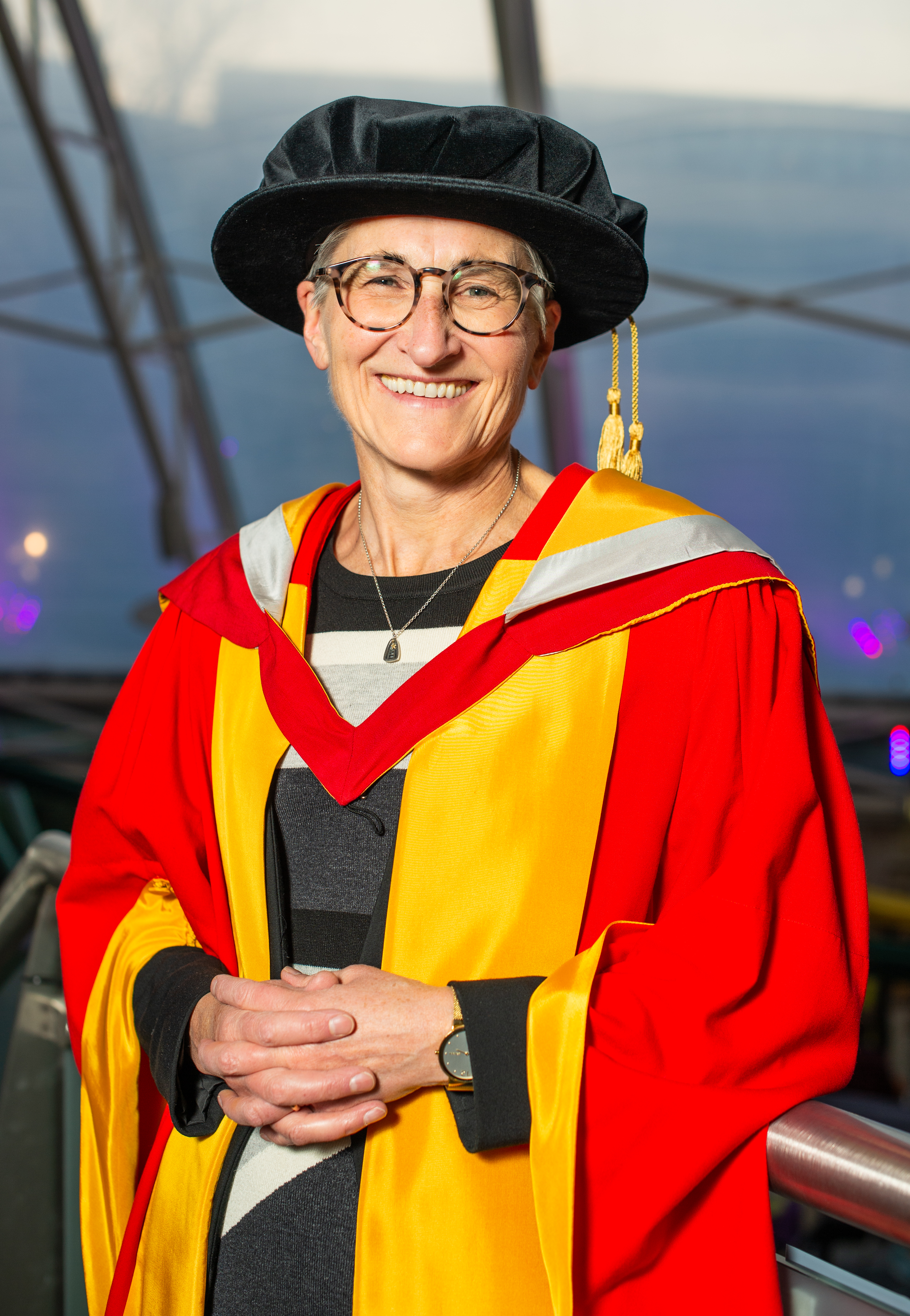 A person in colourful graduation robes, smiling