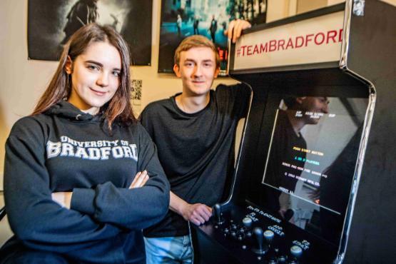 Two students stood next to games arcade machine
