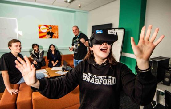 Student in foreground wearing virtual reality headset with arms up