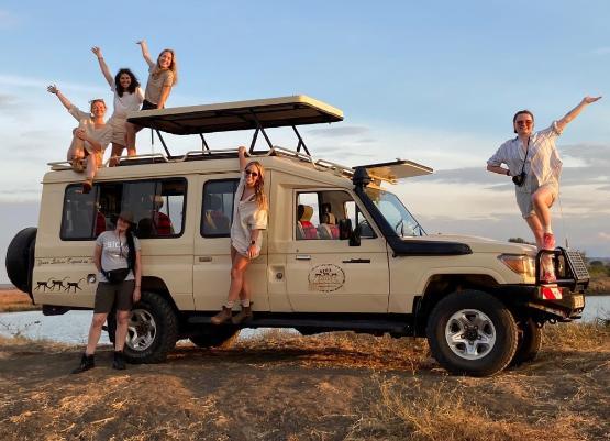 Numerous students all stood waving from a long-wheelbase Land Rover