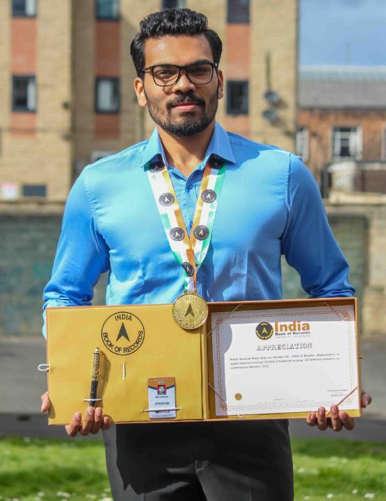 Student wearing a medal holds a box featuring a certificate