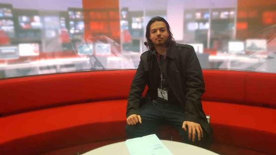 Alumni student sits down on red sofa in TV studio