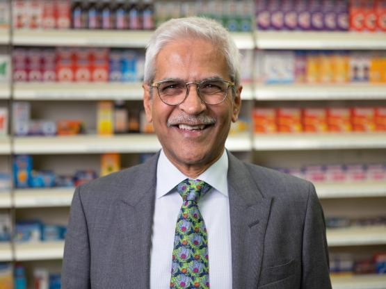 Person wearing suit stands in front of shelves of items inside a pharmacy