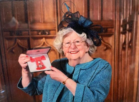 An academic stood up proudly holding an MBE medal in front of wooden panel background