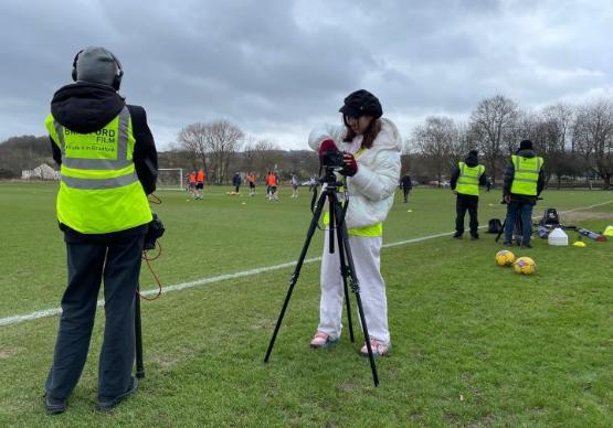 a student with a video camera on a tripod at a football pitch