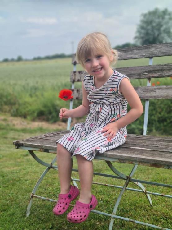 Picture of young person sat on a bench in countryside holding a flower