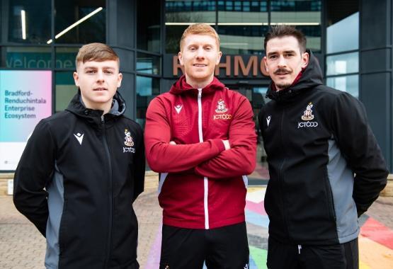 Three football players wearing tracksuits stood together outside university building