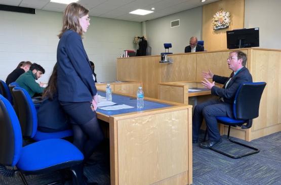 a school student in uniform stood up at in a courtroom cross-examining a person sat in the witness box
